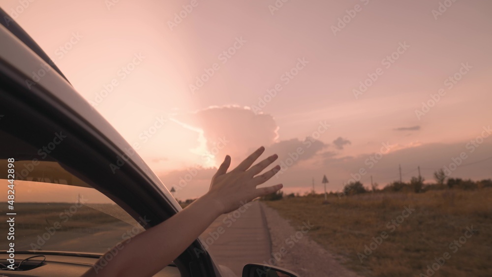 a person's hand is on the car door with an open window, summer vacation in the car at sunset with open arms, a happy girl on a journey get the atmosphere and go to the destination, women vacation