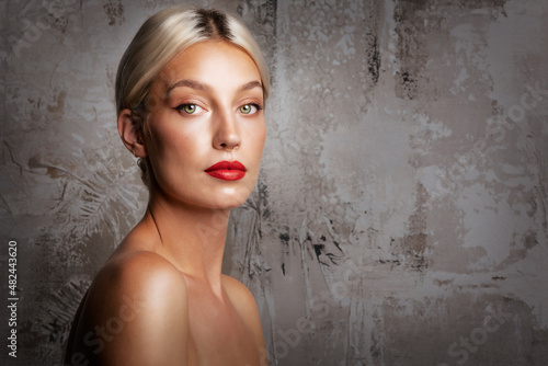 Blond haired beautiful woman wearing red lipstick while standing at isolated dark background