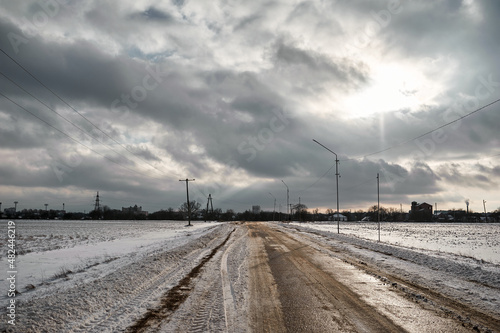 Winter muddy road between fields under clouds © Denys