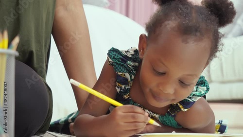 Adorable African American small toddler kid lying in bed with her mom, holding colorful pencils in her hands. loving family spend free time activities, child development concept
