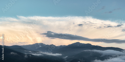 The setting sun illuminates the clouds over the mountain peaks of the caucasus