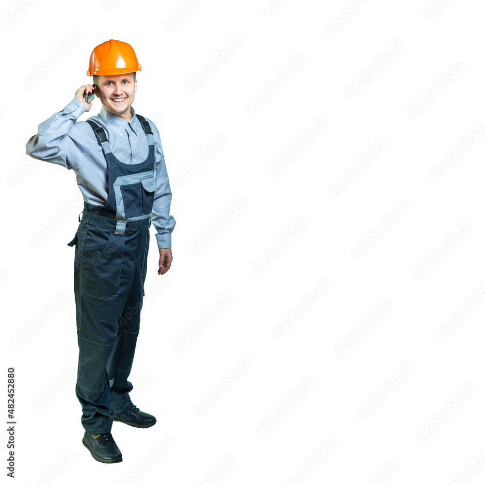 Isolated. Portrait of a worker with overalls and a protective helmet. A cheerful man in overalls receives phone calls. Isolated. Portrait of a worker with overalls and a protective helmet. A cheerful man in overalls receives phone calls.
