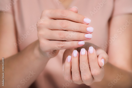 Close up view photography of two beautiful female hands with modern trendy gel polished rounded nails painted with two colors in pink pastel nude look color with cute white small hearts on two nails photo