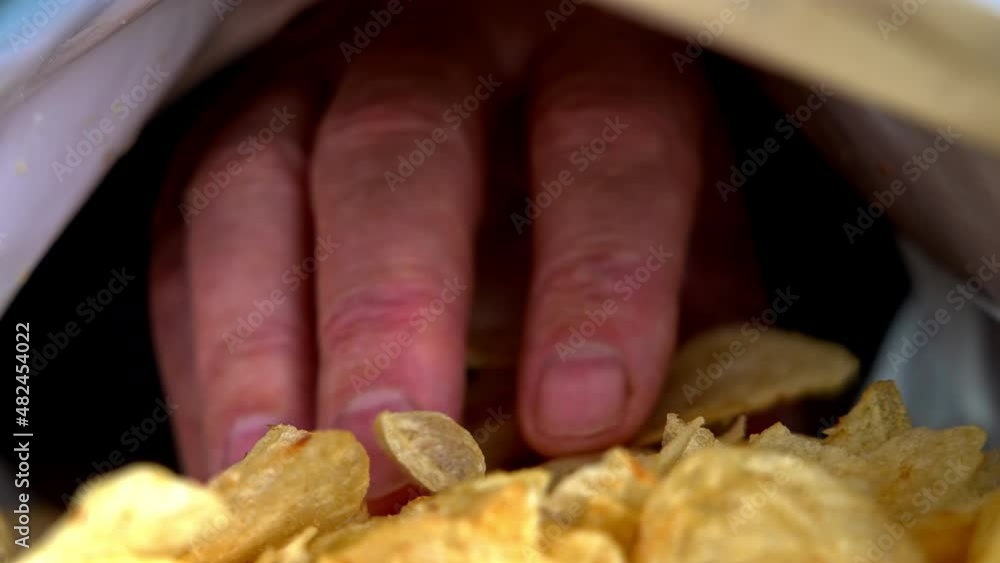 Mans hand is picking potato chips from bag in slow motion, inside view from bag Mans hand is picking potato chips from bag in slow motion, inside view from bag