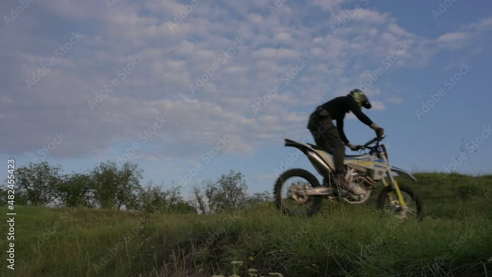 sport man in sportswear and helmet jumping on grass hills on enduro bike motorcycle cross country in slow motion