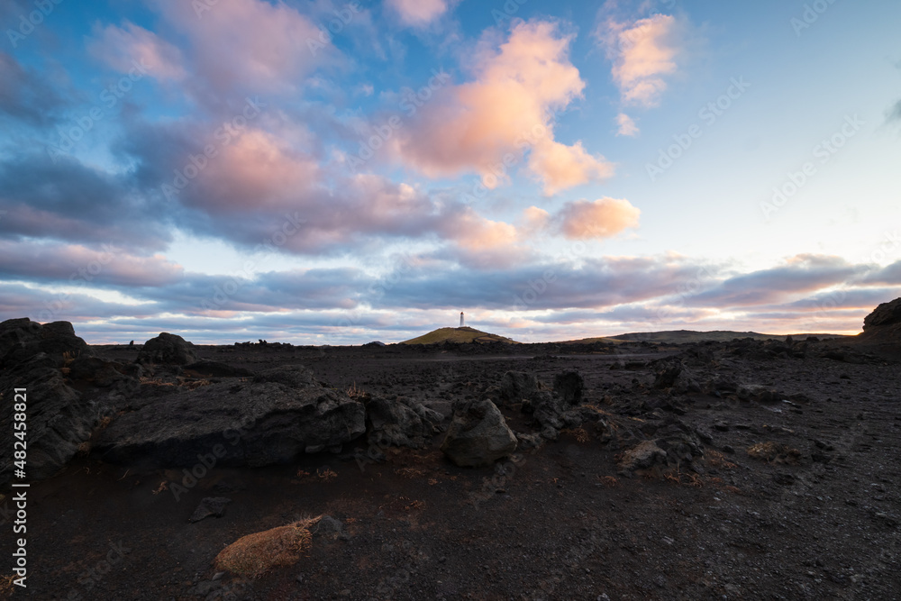 sunrise over a volcanic plain with black rocks and a lighthouse 