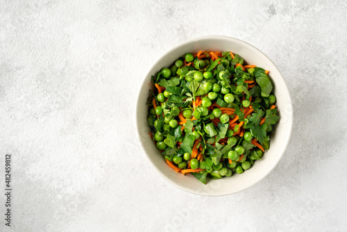 A bowl of salad with green peas, pickled carrots and parsley with olive oil on a bright kitchen table. Delicious healthy salad for health and weight loss. Top view 