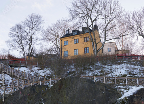 Old yellow 1800s house on the cliff Mariaberget steps climbing up to the board walk Monteliusvägen with scenic view a sunny and snowy winter day in Stockholm  photo
