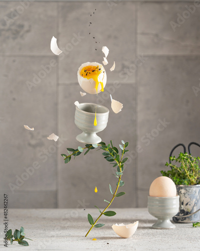 Принти на полотні Levitation art photo of flying cooked egg with yellow yolk drops on white table, shell pieces and greens