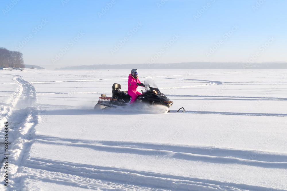 A girl rides a snowmobile through a snow-covered frozen lake. Riding on winter modes of transport. Active recreation. Snowmobiling in winter. Selective focus