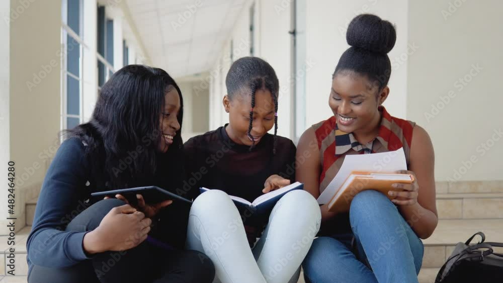 A group of African American students sit on the floor with books and a tablet at the university. Education concept A group of African American students sit on the floor with books and a tablet at the university. Education concept