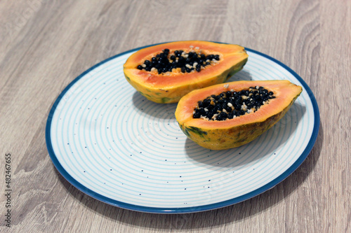 Two slice of ripe papaya on a blue cicled plate with wooden background