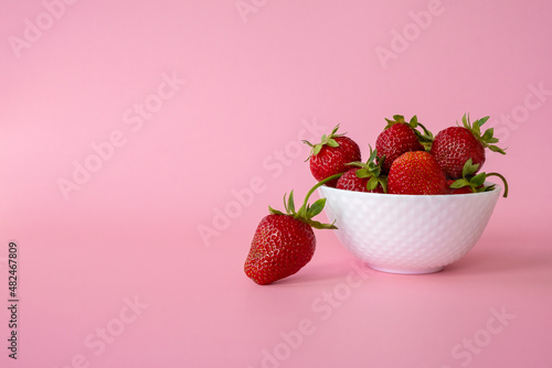 Delicious juicy strawberries in white bowl on pink background. Healthy eating, raw diet and detox food concept. Farm strawberry harvest. Copy space.
