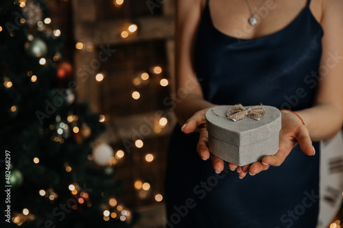 A girl is a woman on the background of a Christmas tree with a gift in her hands. New Year's advertising. Presentation of a gift