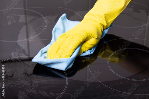A hand in a yellow glove cleans the electric stove from dirt
