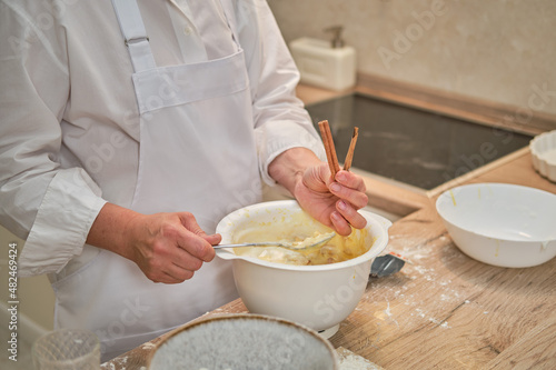 An adult woman in white chef clothes cooking pie in a beige kitchen.