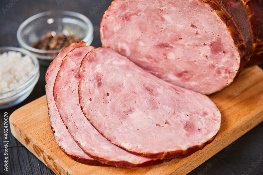 Homemade ham, sliced on a wooden table on a cutting board with spices and salt. Traditional ham homemade, ready to eat, delicious breakfast. The concept of meat products. Homemade ham, sliced on a wooden table on a cutting board with spices and salt. Traditional ham homemade, ready to eat, delicious breakfast. The concept of meat products.