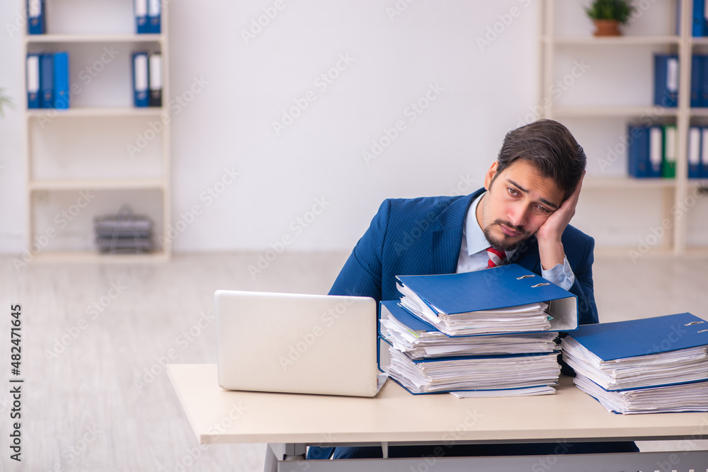 Young male employee unhappy with excessive work in the office Young male employee unhappy with excessive work in the office