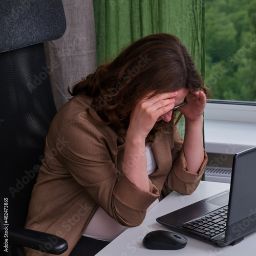 Pregnant woman with laptop in home office crying holding her head