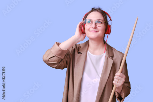 Smiling woman teacher listening to music in red headphones on blue background, copy space photo