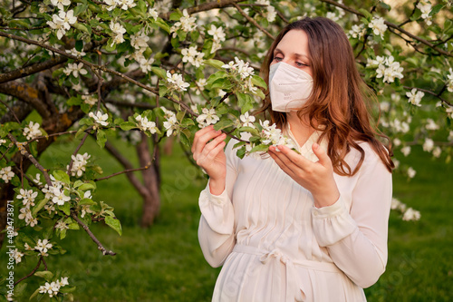 Pregnant woman in medical face mask n95 with apple tree flowers in spring nature. Happiness of pregnancy during covid epidemic  coronavirus pandemic quarantine