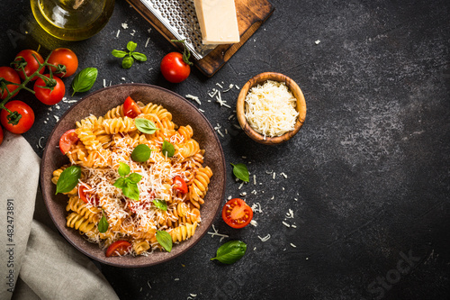 Traditional Italian pasta with tomato sauce, basil and parmesan on black table. Fusilli pasta with tomato sauce arrabbiata. Top view.