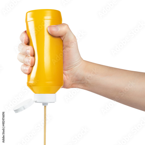 Hand squeezing mustard out of a plastic bottle, isolated on white background photo