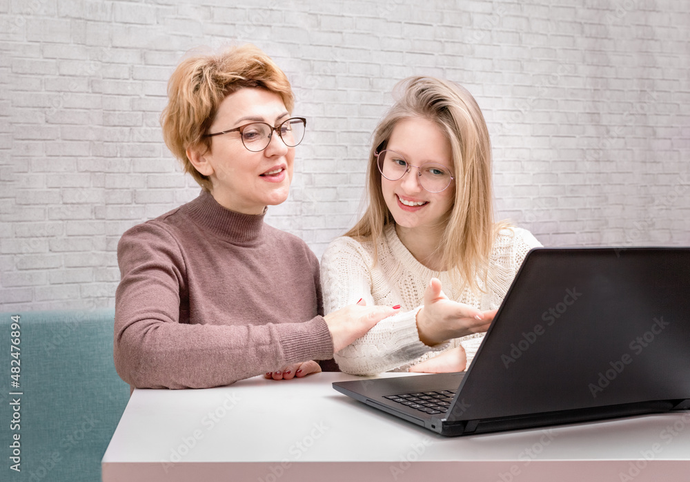 Cute smiling teen girl and mother using laptop in the house. Mother and Daughter at Home. Teenage Girl. Cute smiling teen girl and mother using laptop in the house. Mother and Daughter at Home. Teenage Girl.