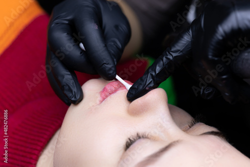 the master performs the procedure of permanent makeup of the lips erase the remnants of the tattoo pigment with a cotton swab to continue the tattoo procedure