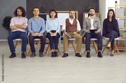 Group of young people are sitting at a job interview in the office. Senior and young men and women are waiting for an interview  sitting in a line on chairs  waiting for an interview with a company.