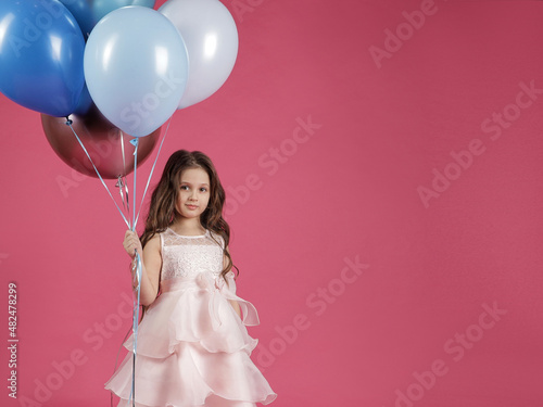 A little cute girl stands on a pink background and holds balloons,a place to copy