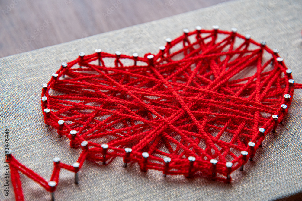 Craft string art in shape of heart. Red woolen heart, symbol of love, made  of red wool yarn threads tangled over metal nails on canvas background  Stock Photo | Adobe Stock