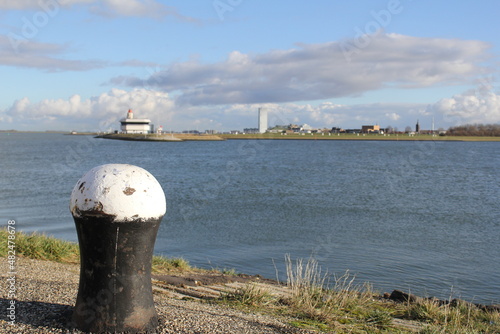 The estuary of the canal Ghent Terneuzen in the westerschelde sea and the skyline of Terneuzen in the background and a bollard at the quay in front and a blue sky photo