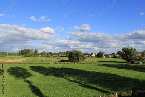 a typical dutch landscape with an old green grassland with ditches and trees and a little village 'Vogelwaarde' in zeeland and blue sky with white clouds in the background