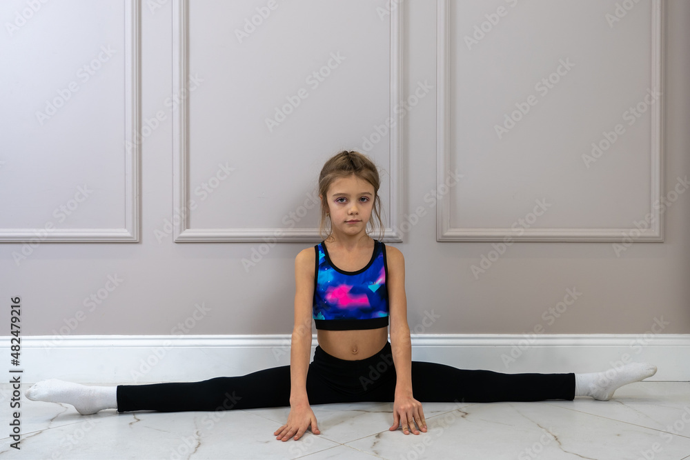 little girl in sports clothes doing split on the floor in a living room