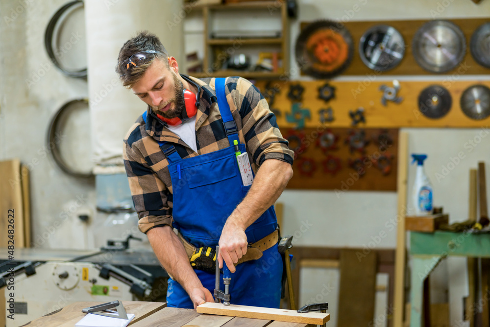 Young handsome caucasian carpenter working with clamps in workshop Young handsome caucasian carpenter working with clamps in workshop