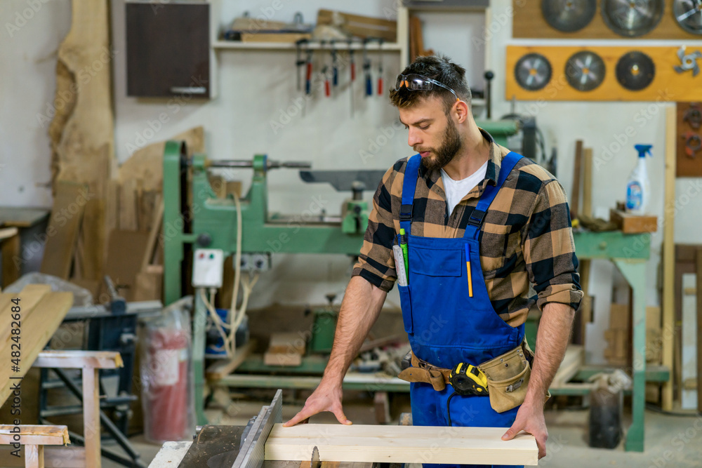 Handsome carpenter preparing, measures and cutting boards on cutting machine Handsome carpenter preparing, measures and cutting boards on cutting machine