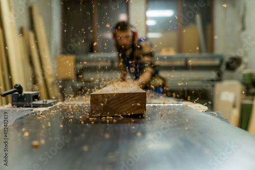 Bearded carpenter working on machine for straighten wood boards photo