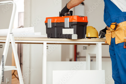 Cropped shot of contractor worker in overalls putting toolbox on the table, ready for construction work