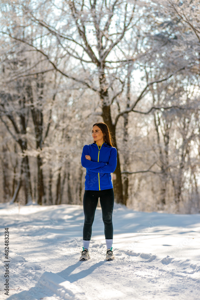 Beautiful Caucasian brunette in sportswear stands on a country road covered with snow and posing for camera. Portrait time