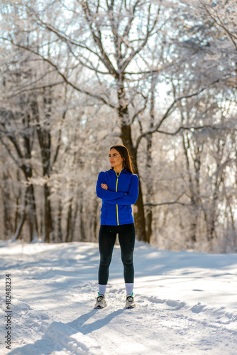 Beautiful Caucasian brunette in sportswear stands on a country road covered with snow and posing for camera. Portrait time