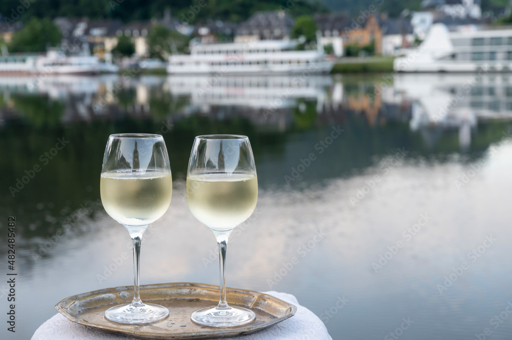 Obraz premium Tasting of white quality riesling wine served on outdoor terrace in Mosel wine region with Mosel river and old German town on background, Germany