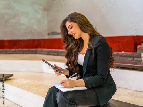 Young attractive business woman using a digital tablet and writing in her notebook