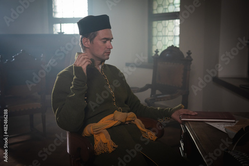 Portrait of a man in a medieval costume. A scribe writes on a red table. Retro style and historical clothes concepts photo