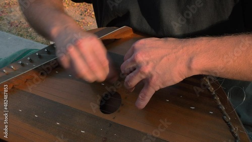 Musician hands beat the strings rhythmically. A man holds gusli on his lap and plays. Soft daylight. Close-up.