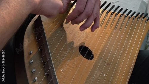 Musician hands beat the strings rhythmically. A man holds gusli on his lap and plays. Soft daylight. Close-up.