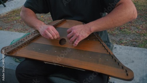 Musician hands beat the strings rhythmically. A man holds gusli on his lap and plays. Soft daylight. Close-up.