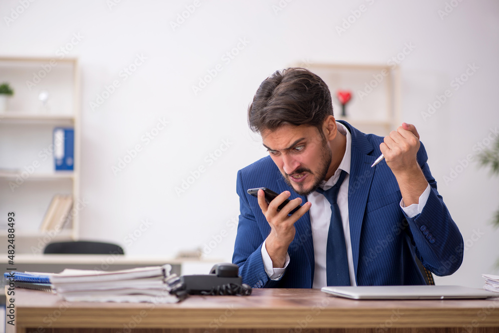 Young male employee unhappy with excessive work in the office Young male employee unhappy with excessive work in the office