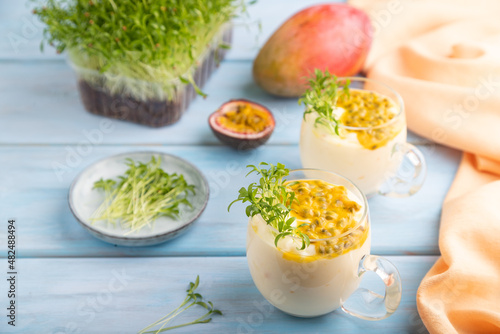 Mango yogurt with passionfruit and cilantro microgreen in glass on blue. Side view, selective focus.