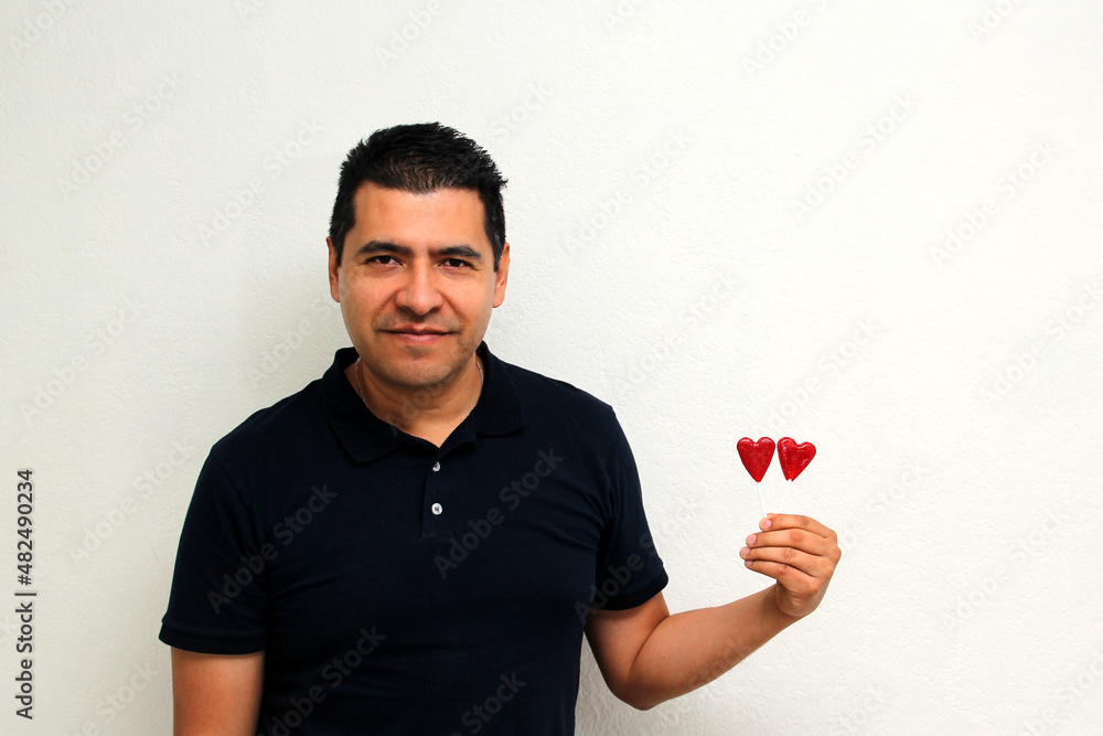 Latino adult man with heart-shaped candy lollipops shows his enthusiasm for the arrival of February and celebrate Valentine's Day of Love and Friendship with his partner, friends and family
Latino adult man with heart-shaped candy lollipops shows his enthusiasm for the arrival of February and celebrate Valentine's Day of Love and Friendship with his partner, friends and family